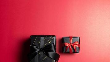 vista superior de la caja de regalo negra con cintas rojas y negras aisladas en el fondo rojo. foto