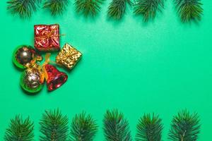 Top view of Christmas gift box red balls with spruce branches and bell on green background. photo