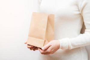 Close up female holds in hand brown clear empty blank craft  eco paper bag on white background. photo