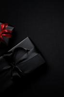 black gift box with red and black ribbons isolated on black background photo