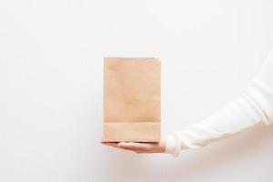 Close up female holds in hand brown clear empty blank craft  eco paper bag on white background. photo