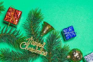 Top view of Christmas gift box red balls with spruce branches and bell on green background. photo