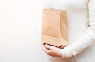 Close up female holds in hand brown clear empty blank craft  eco paper bag on white background. photo