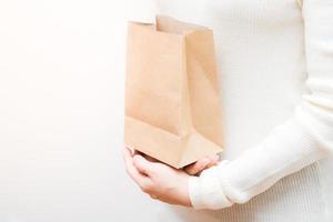 Close up female holds in hand brown clear empty blank craft  eco paper bag on white background. photo