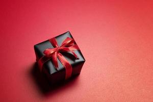 Top view of black gift box with red and black ribbons isolated on red background. photo