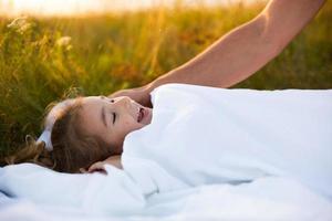 Girl sleeps on white bed in the grass, fresh air. Dad's hand gently pats his head. Care, protection, International Children's Day, mosquito bites photo