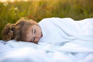 The girl sleeps on white bed linen in nature in the grass, in the fresh air. Protection from mosquitoes, healthy sleep, the benefits of ventilation, hardening, clean nature, ecology, children's health photo