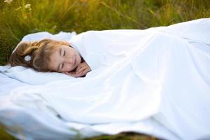 The girl sleeps on white bed linen in nature in the grass, in the fresh air. Protection from mosquitoes, healthy sleep, the benefits of ventilation, hardening, clean nature, ecology, children's health photo