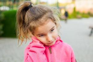 A little girl in a pink hoodie with a sad and tearful face is holding her ear. Ear pain, otitis media, swelling of the cheek, gums, toothache, children's surgery, otolaryngology. Children's medicine photo