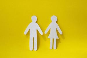 Silhouettes of a man and a woman are carved from white paper, standing side by side on a yellow background. The concept of love, relationships, family photo