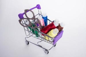 Mini decorative shopping cart with with colored threads for sewing and scissors on white background. photo