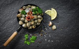 berberechos plato de marisco con hierbas y especias sobre fondo oscuro - berberecho de sangre pelado en la sartén foto