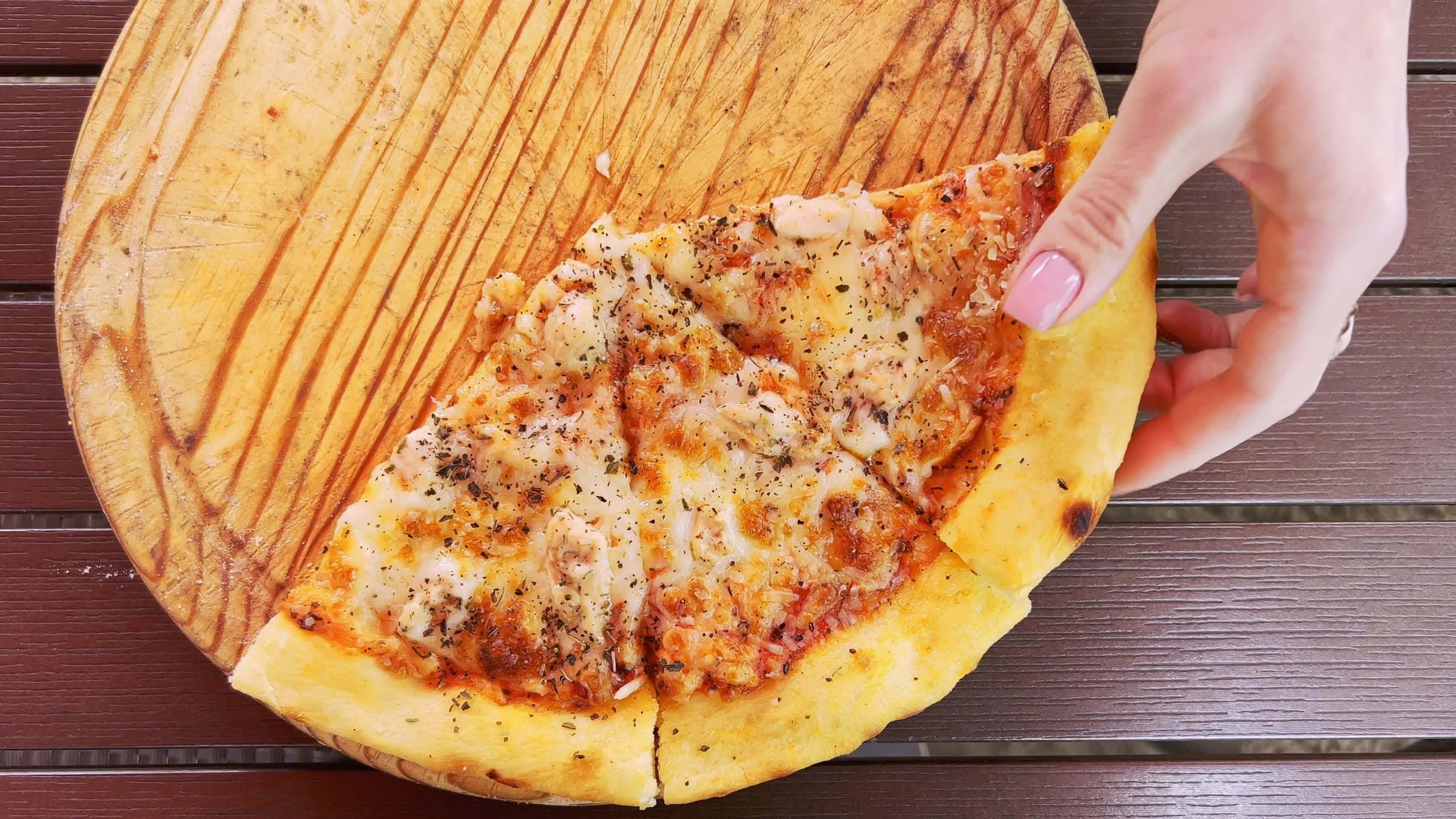 A womans hand breaks a slice of hot, fragrant pizza lying on a wooden tray.
