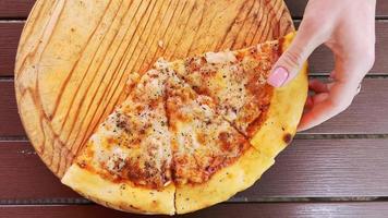 A woman's hand breaks a slice of hot, fragrant pizza lying on a wooden tray. video