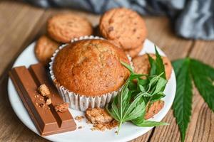 galletas de comida de cannabis con pastel de chocolate hoja de cannabis hierba de marihuana sobre fondo oscuro y de madera, deliciosa galleta dulce de postre con planta de hoja de cáñamo thc cbd hierbas comida snack y vista superior médica foto