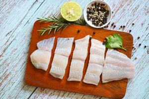 fresh raw pangasius fish fillet with herb and spices black pepper lemon lime and rosemary, fish fillet on wooden board with ingredients for cooking, meat dolly fish tilapia striped catfish photo