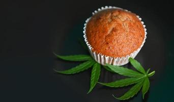 Cannabis food cake with cannabis leaf marijuana herb on dark background, delicious sweet dessert cupcakes with hemp leaf plant THC CBD herbs food snack and medical photo