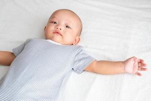 el ángulo de visión es un bebé que lleva una camisa a rayas. Acuéstese con las piernas levantadas y los brazos extendidos. sobre el colchón blanco foto
