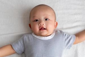 Baby boy wearing a striped shirt smiling on a white carpet photo