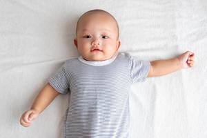 A baby in a striped shirt lies smiling on the white carpet. photo