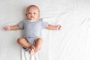 The top view image has a side area , is a baby boy wearing a striped shirt. Lie with your legs up and your arms outstretched on the bed. photo