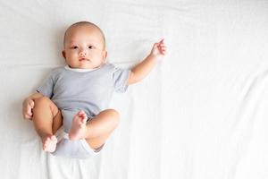 vista superior bebé con una camisa a rayas, levantando los brazos y las piernas sobre una alfombra blanca. foto