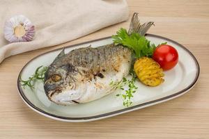 Grilled dorado on the plate and wooden background photo