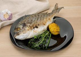 Grilled dorado on the plate and wooden background photo