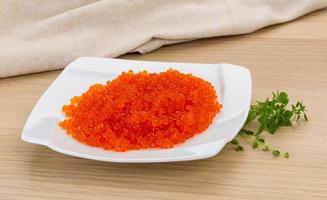 Red caviar on the plate and wooden background photo