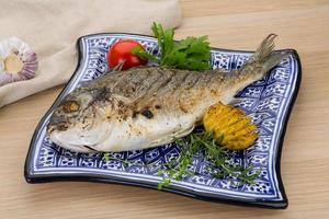 Grilled dorado on the plate and wooden background photo