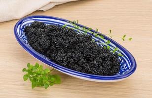 Black caviar in a bowl on wooden background photo