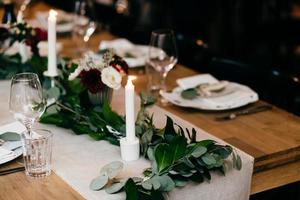 Banquet table setting. Plates, forks, candles on wooden table with nice decoration. Cutlery and wine glasses. Restaurant cozy interior. Table served for special occasion. Celebration concept photo
