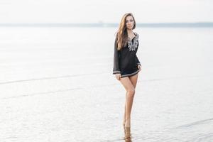 foto al aire libre de una mujer bonita con forma corporal perfecta, se encuentra en la costa contra el fondo del mar, se ve con expresión determinada, disfruta de un ambiente tranquilo durante las vacaciones de verano en la costa