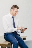 Pleased attractive young businessman checks email on portable pc, watches vidio on internet webpage, uses free internet connection, wears elegant formal clothes, isolated over white background photo