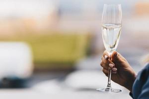 la mano de la mujer sostiene una copa de vino blanco, celebra algo junto con amigos, fondo borroso con espacio para copiar su texto promocional o publicidad. foto