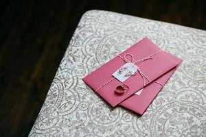 anillos de boda sobre una tarjeta de invitación rosa. preparativos y decoraciones para bodas. tarjeta de boda hecha por el novio y la novia. concepto de amor y romance foto