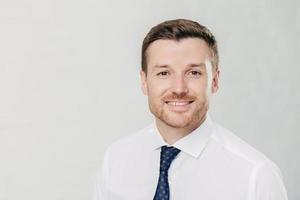 Headshot of attractive unshaven young male with cheerful expression, looks confidently at camera, being pleased to meet with colleagues, dressed in formal clothes, isolated over white background photo