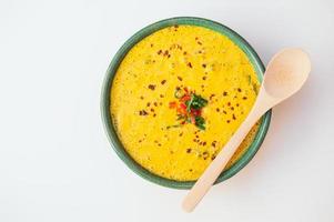 Hot creamy delicious soup with greenery and vegetables, wooden spoon on bowl, isolated over white background. Coconut curry soup. Fresh disn. Healthy eating concept photo