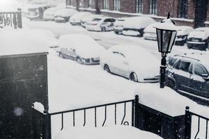 Driving in snow. Cars covered with snow stand in parking lot, being paralysed because of bad weather conditions. Street after heavy snowstrom. Transportation concept photo