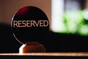 el cartel de la mesa indica mesa reservada en el restaurante se encuentra contra el fondo borroso del café. concepto de reserva. una etiqueta de reserva. beige sobre mesa de madera.