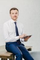 Vertical shot of serious businessman uses modern tablet computer for reading financial news online, makes banking, browses web page, connected to wireless internet. People and technology concept photo