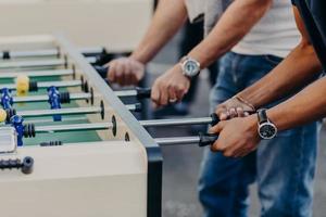 Cropped view of males hands play table football, enjoy recreation or leisure time during holidays, spend free time in bar. Competition concept photo