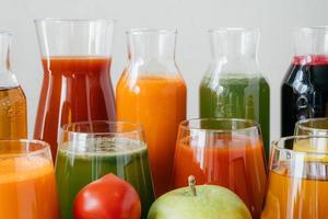 primer plano de botellas de vidrio llenas de jugo colorido hecho de varias verduras y frutas, tomate rojo y manzana verde en primer plano. bebida fresca de desintoxicación foto