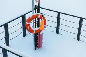 Lifebuoy against snow background. Life preserver next to frozen winter pond or river covered with hoarfrost. Frosty winter day. Risk and protection concept photo