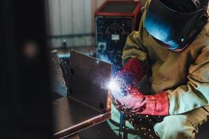 Welding concept. Industrial worker or welder wears protective mask and gloves erects technical steel on factory. Labour worker welds metal. Man repairs detail in cars auto service. Steel worker photo