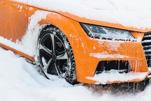View of orange car covered with snow, stands on road, frozen on frost. Winter and transportation concept. Automobile on street. Weather conditions photo