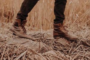 zapatos marrones para hombre en territorio rural. masculino irreconocible en pantalones y botas. calzado antiguo de cuero. caminar al aire libre foto