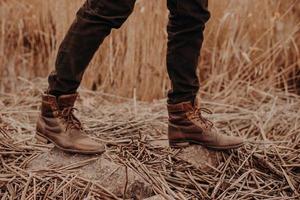 Cropped shot of unrecognizable man wears old leather brown footwear, poses on ground with stubble, walks at field alone. photo