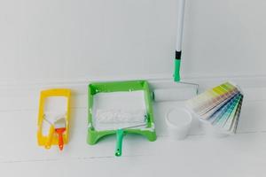 Photo of two trays with paint rollers, bucket with color and colour samples, white background. House renovation concept. Refurbishment