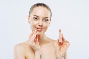 Isolated shot of beautiful girl applies lipstick on lips, has perfect makeup, poses with beauty product, touches face gently, poses shirtless, gets ready for work, poses against white background photo